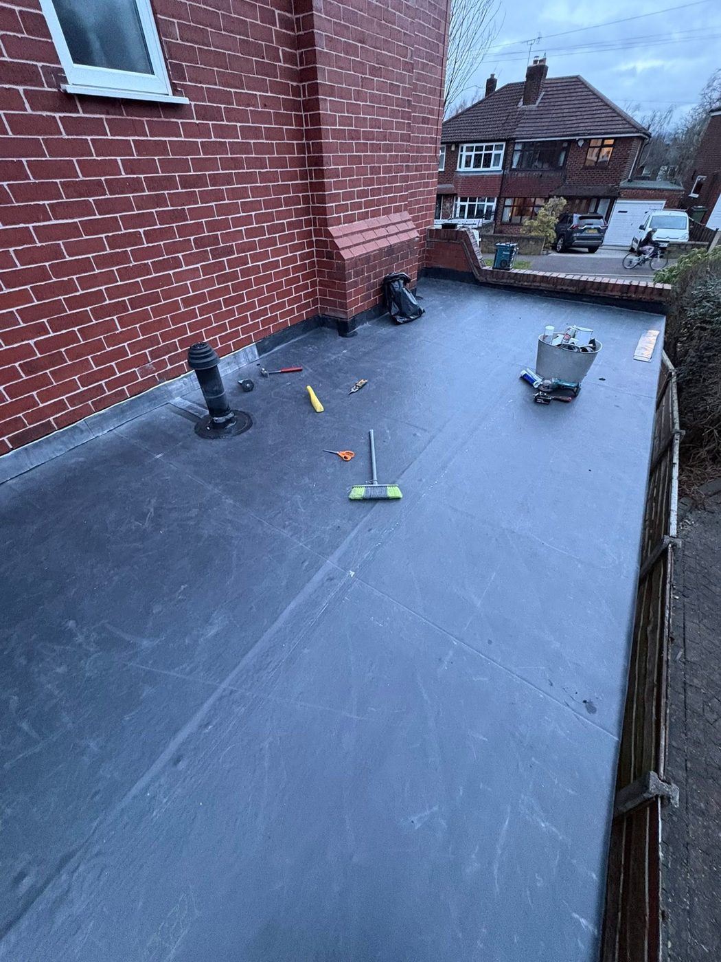 Completed seamless Firestone EPDM rubber flat roof on a rear extension, with the dark grey membrane dressed up the brickwork and a soil vent pipe collar installed
