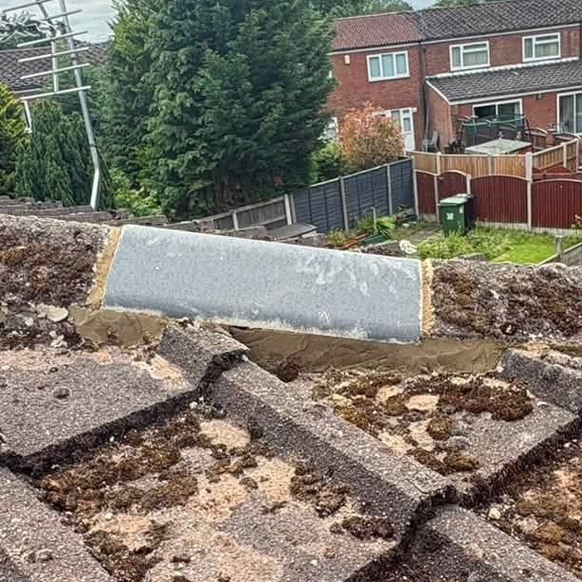 A replaced ridge tile bedded into fresh mortar along the ridge of a weathered concrete tiled roof, the new tile clearly lighter than the mossy tiles either side