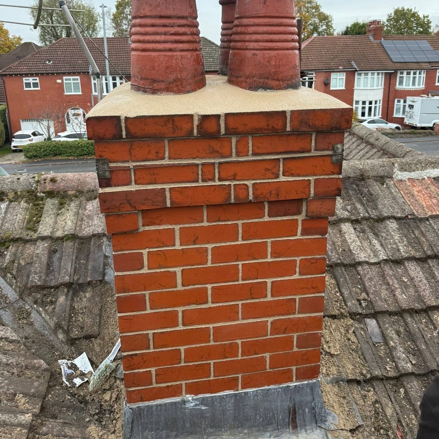 Fully rebuilt chimney stack in fresh red brick with clean mortar joints, new sand and cement flaunching to the top, the original clay pots refitted and new lead flashing dressed in at the base where the stack meets the tiles